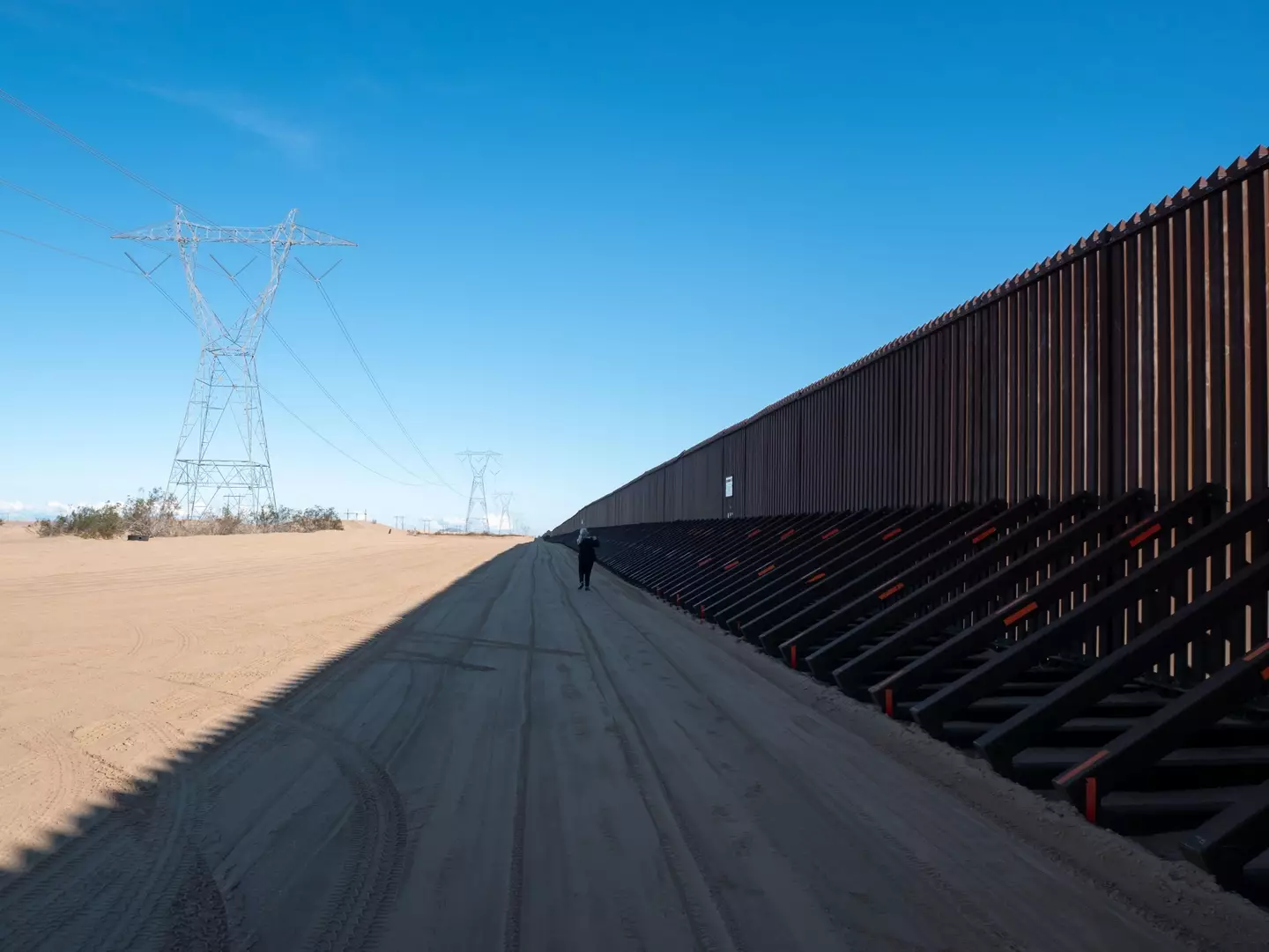 Person walks alongside the US/Mexico border wall.