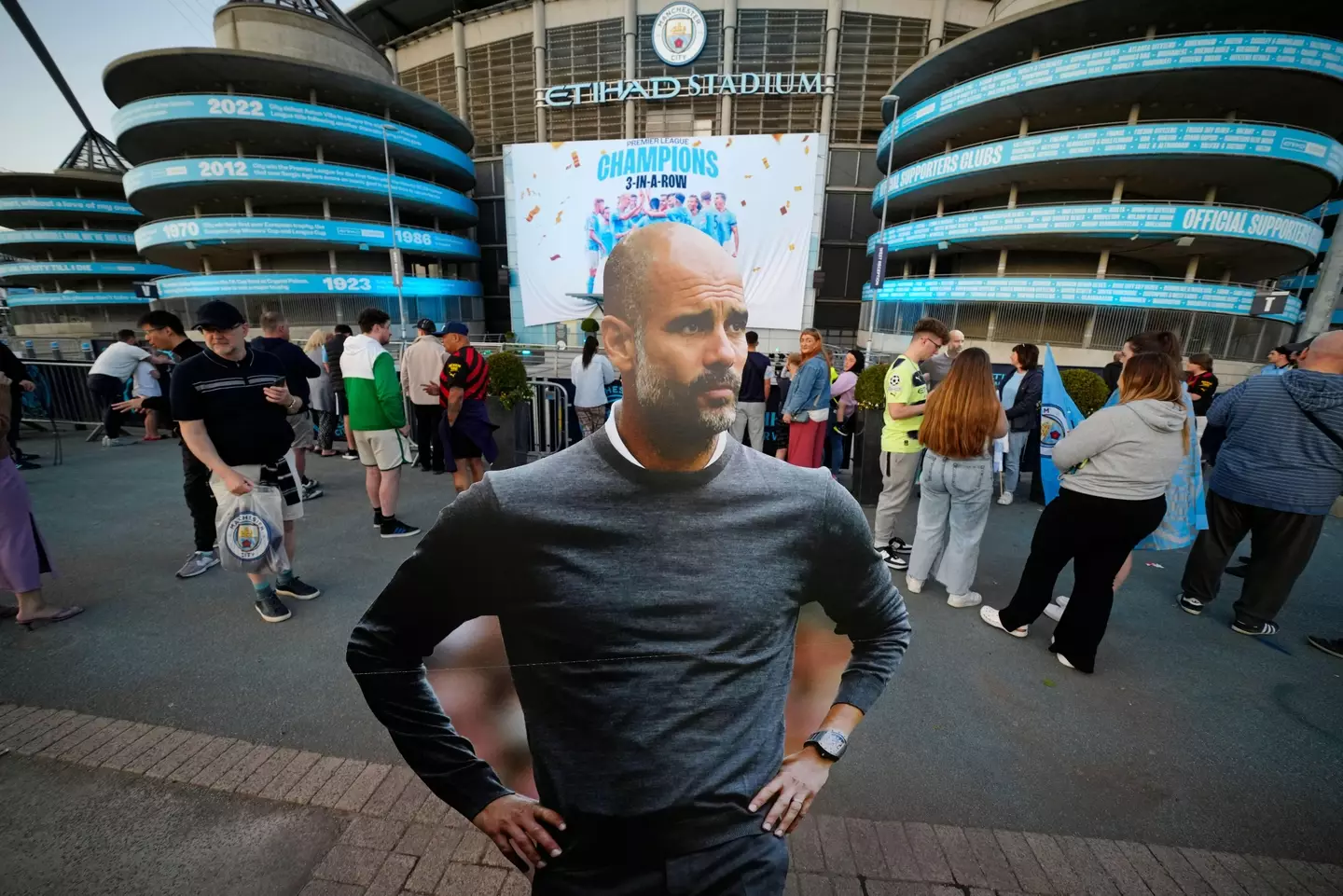 A Pep Guardiola cut-out stands in front of the Etihad as a crowd gathers. Image: Alamy