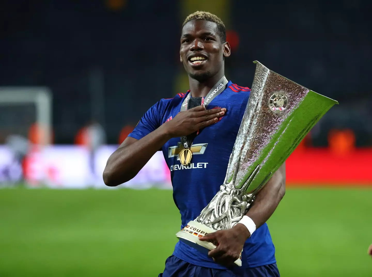 Paul Pogba tapping the Manchester United crest and holding the UEFA Europa League trophy after scoring in the 2017 final against AFC Ajax.