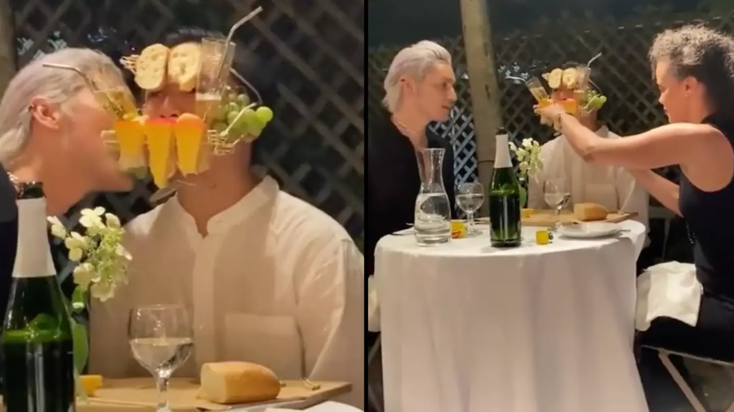 Man holds cheese board in mouth at dinner table while people eat off his face