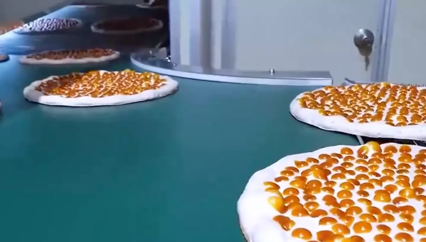 The pizza travels down a conveyer belt.