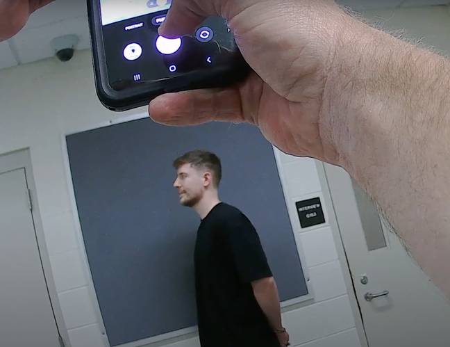 MrBeast having his mugshot taken while a police officer snaps a photo. Credit: Airrack/YouTube