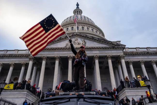 A man waves a flag in front of the Capitol Building during the storming of the building. Credit: Rise Images/Alamy Stock Photo