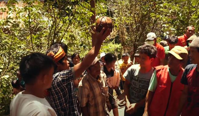 A Torajan man holds up his relative's skull as part of the Walking Dead ritual.  Photo credit: YouTube/Fearless&Far
