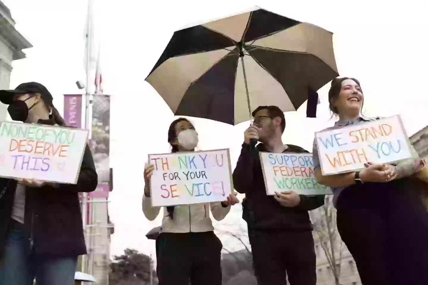 Protestors hold signs as people gather outside the Ronald Reagan Building during a 'clap out' in support of USAID staff that were fired (TING SHEN/AFP via Getty Images)