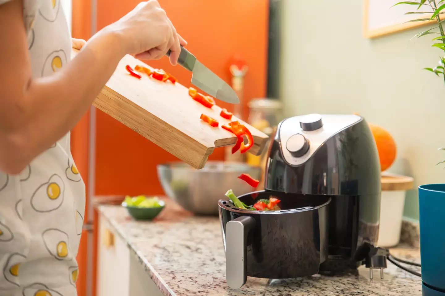 Woman puts chopped vegetables in an air fryer - Pavlina Popovska via Getty Images