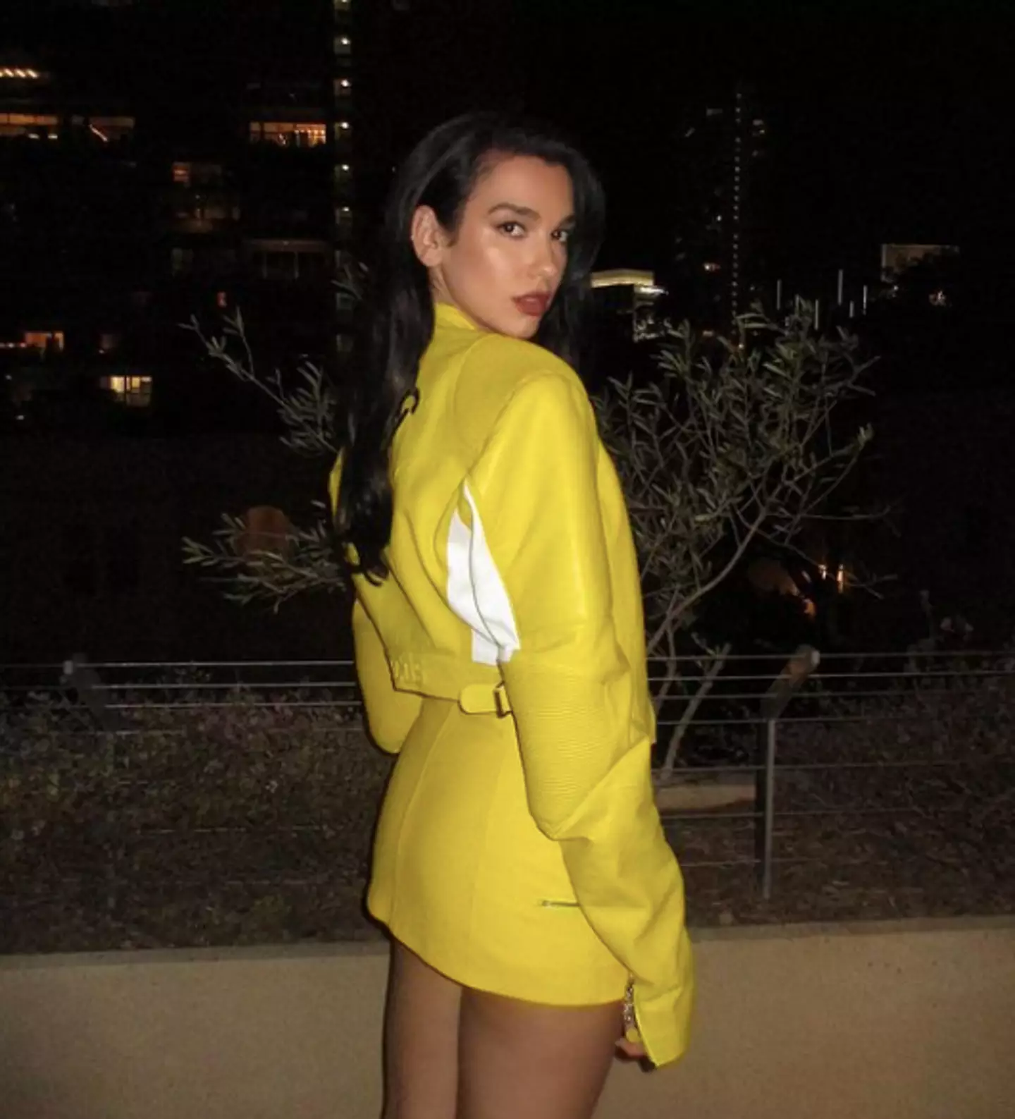 Dua Lipa looks at the camera posing in a yellow jacket and skirt.