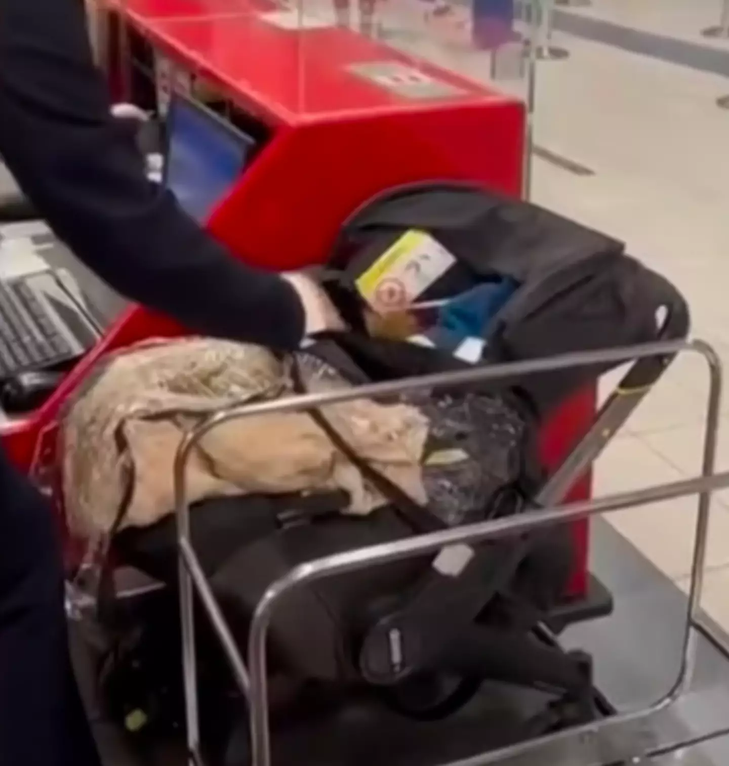 Footage shows airport staff peeling back the blanket lying on top of the baby carrier to find a baby lying underneath.