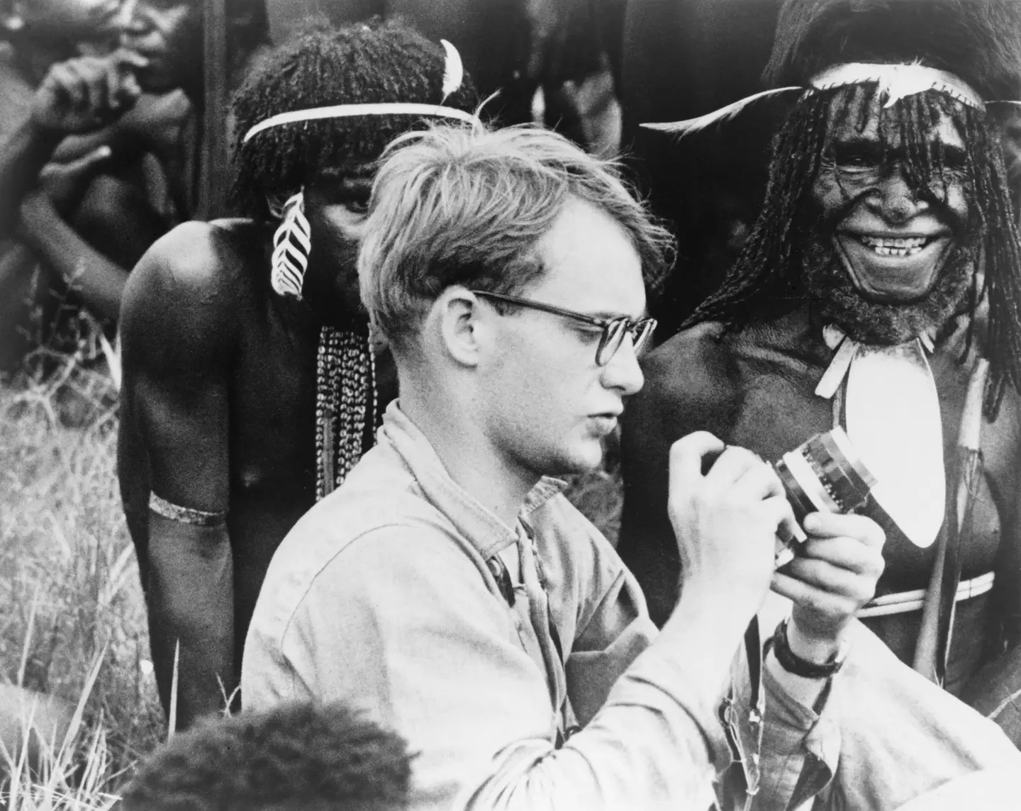 Michael C. Rockefeller (1934-1961) adjusting his camera in New Guinea, Papuan men in background. This is one of the last pictures of him alive.