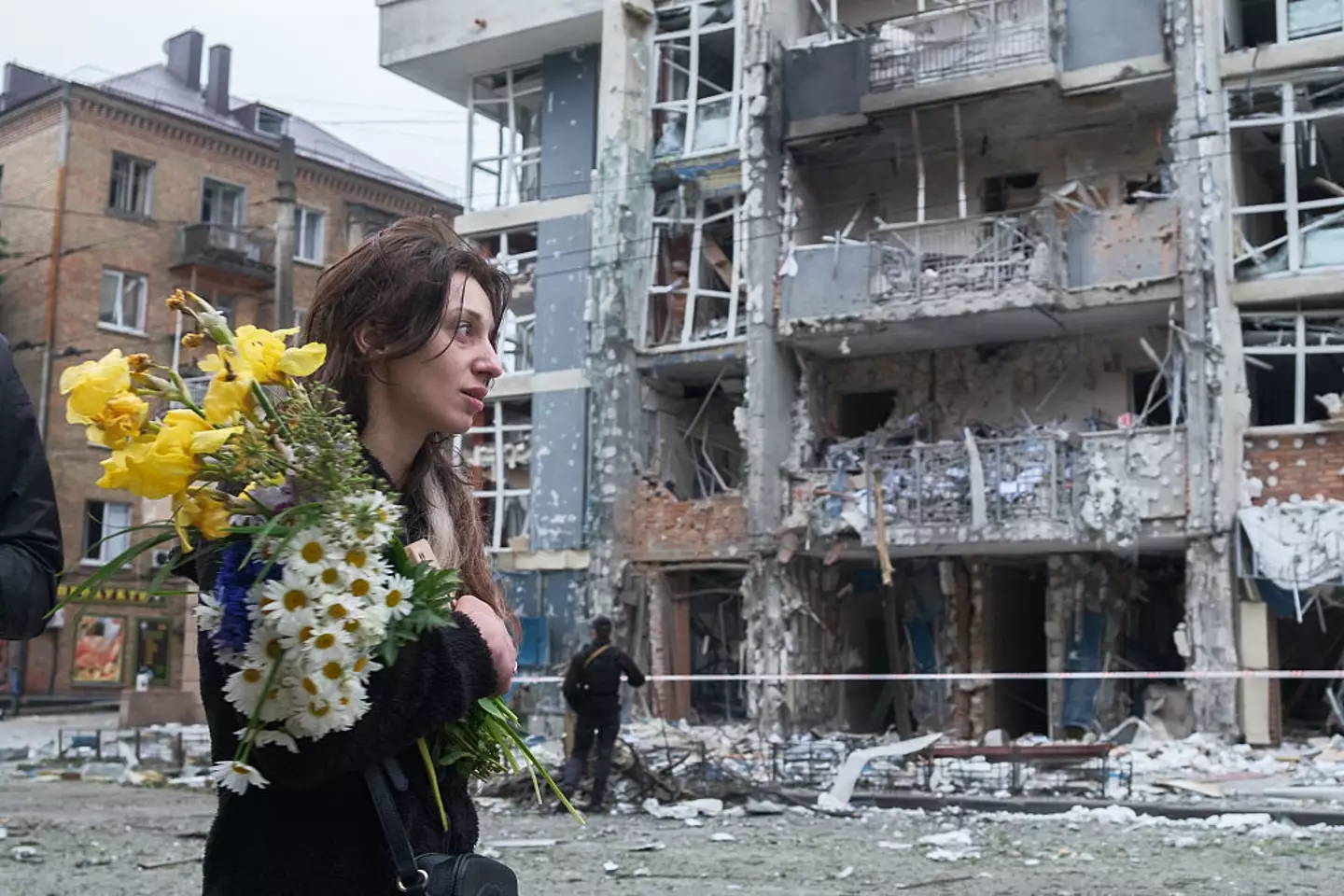 War is still raging on in Eastern Europe, as a woman is pictured with a bouquet of flowers walks past a high-rise residential building in the Shevchenkivskyi district of Ukraine heavily damaged by a Russian drone strike this week (Vitalii Nosach/Global Images Ukraine via Getty Images)