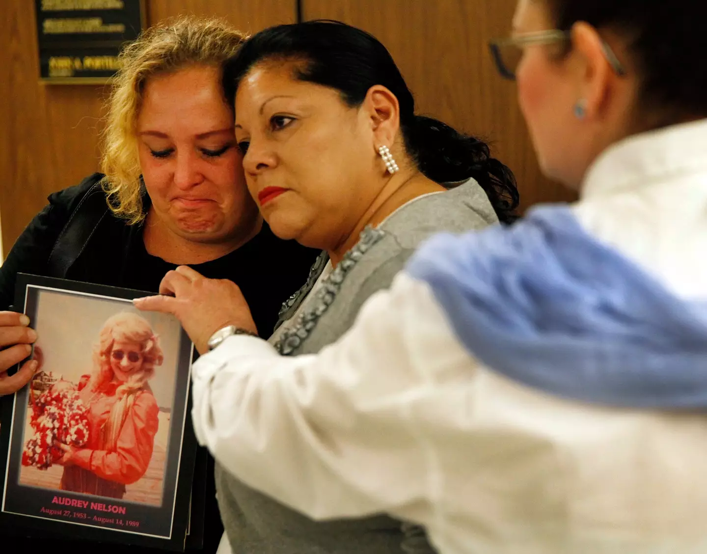 Pearl Nelson (left) holding a photo of her mother, victim Audrey Nelson, as she is hugged by Mary Louise Frias, whose Godmother, Guadalupe Apodaca Zambrano was also a victim of the convicted serial killer.