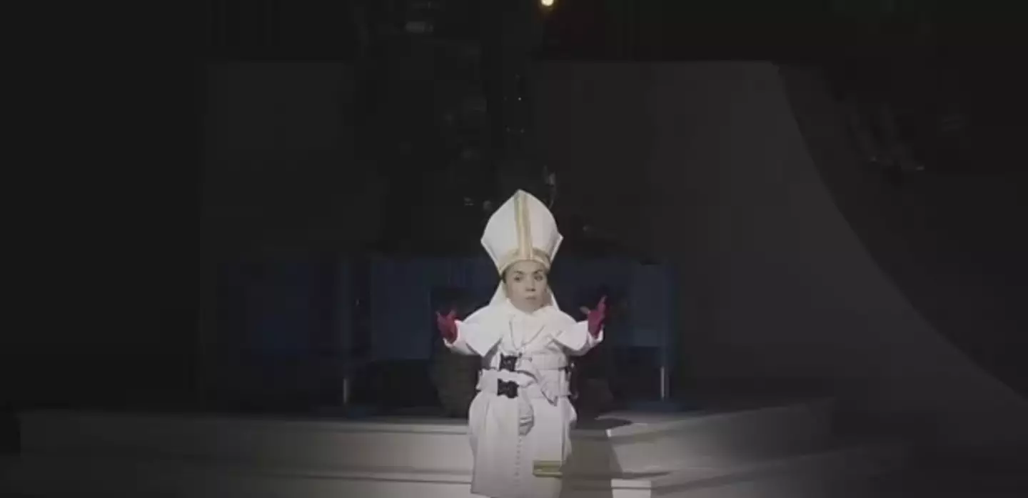 An actress with dwarfism dressed as a nun is swung around my a mechanical arm (YouTube/Staatsoper Stuttgart)