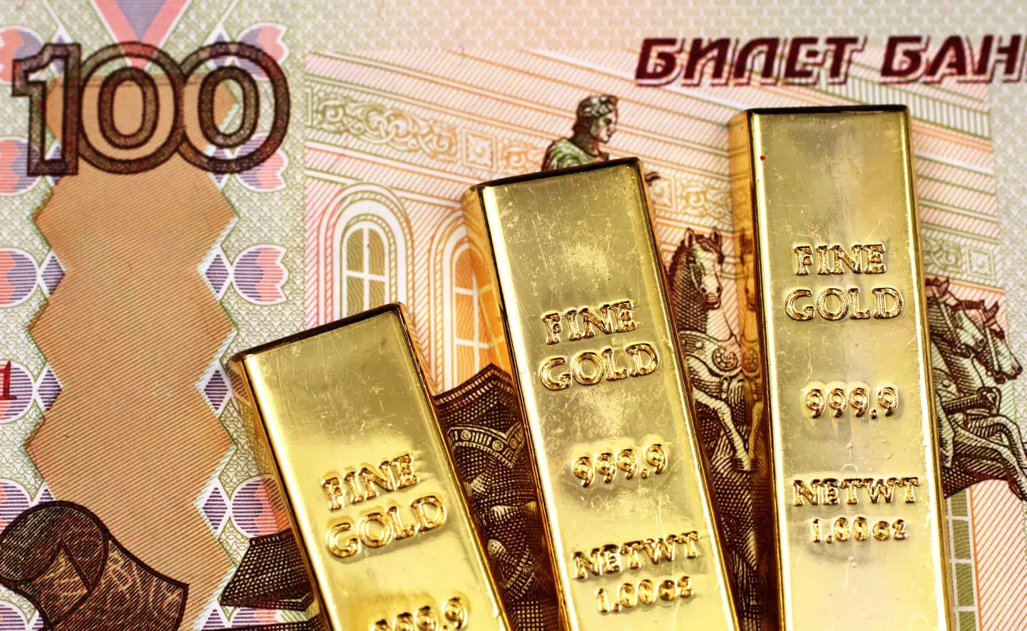 A hundred Russian ruble bank note with three small golden ingots in macro close up.