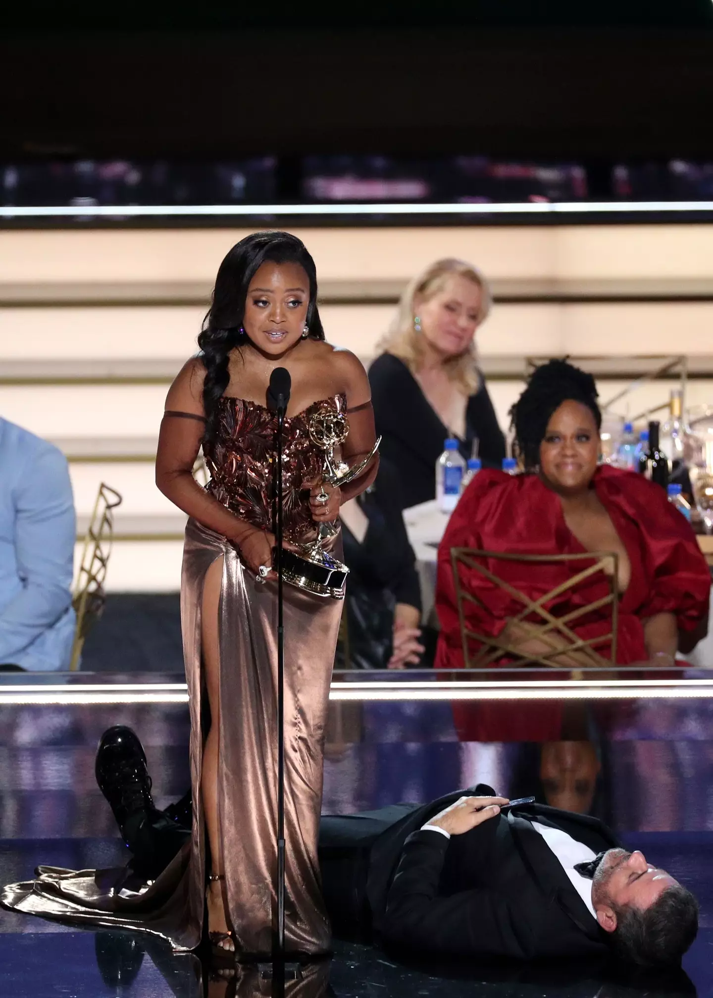 Quinta Brunson accepting her award with Jimmy Kimmel laying by her feet, seemingly passed out.