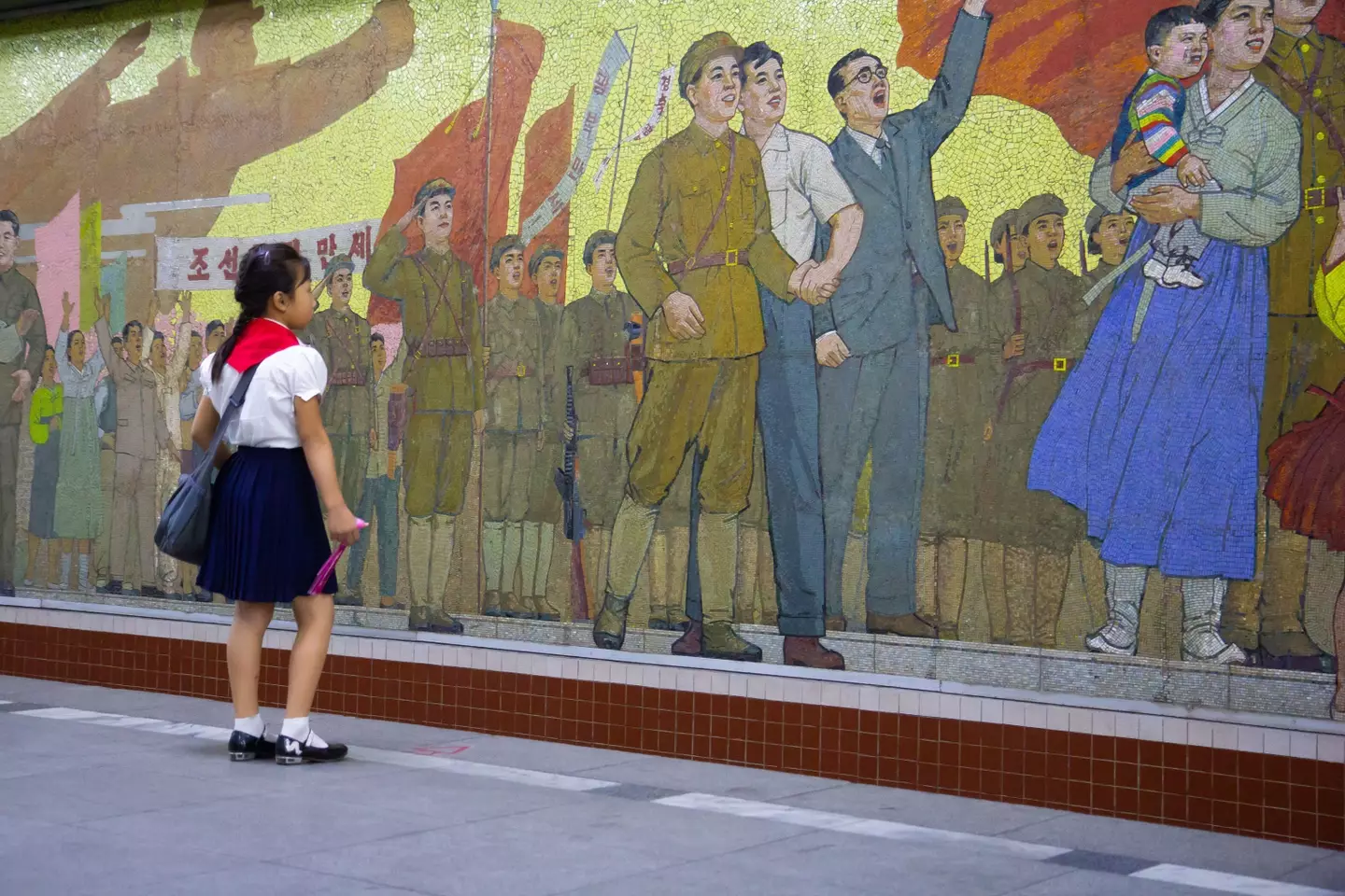 A school girl in front of a socialist realist mosaic at Pyongyang Metro in North Korea.