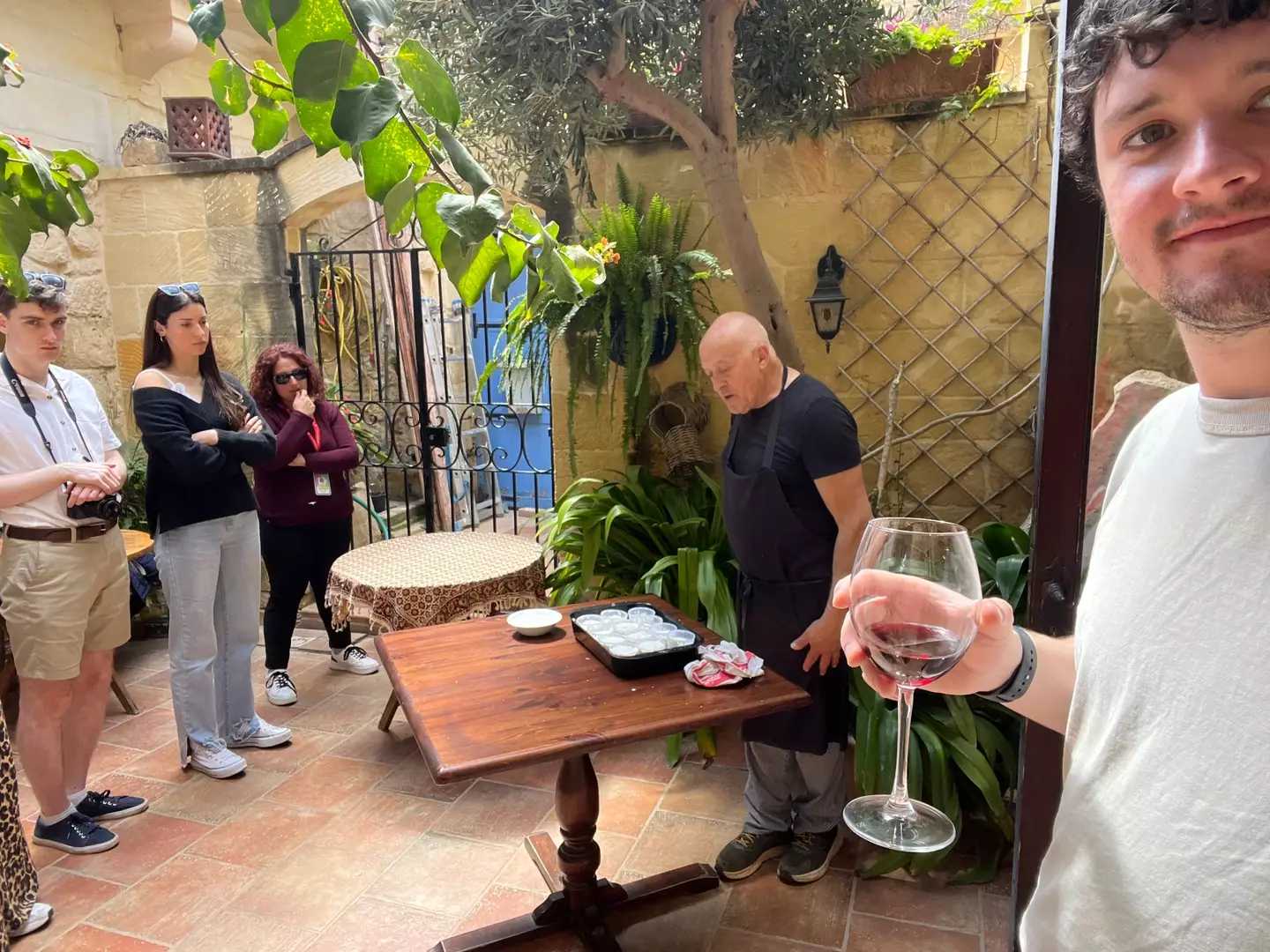 Joe pictured enjoying a glass of red wine while watching Martin, the owner of Il-Wileġ restaurant, make cheese (LADbible)
