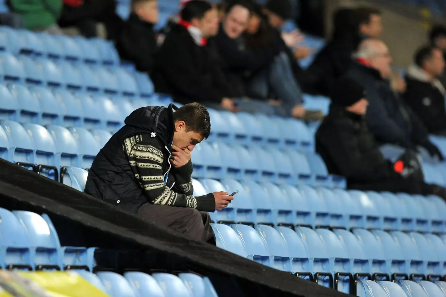 A Morecambe fan on his phone in the stands of the Ricoh Arena |