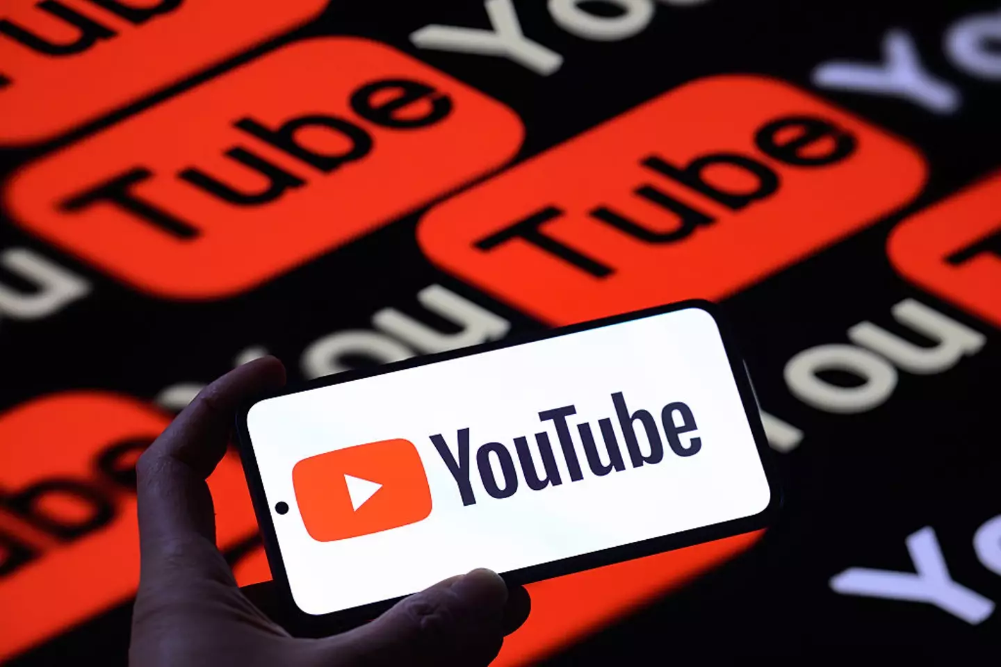 The YouTube logo is displayed on a mobile phone with YouTube seen in the background (Getty Images)