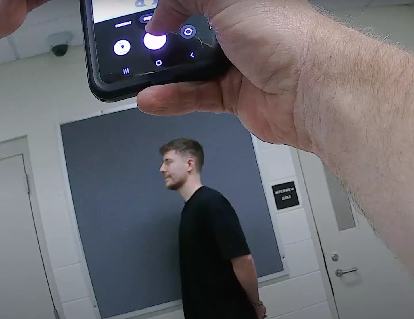 MrBeast having his mugshot taken while a police officer snaps a photo.