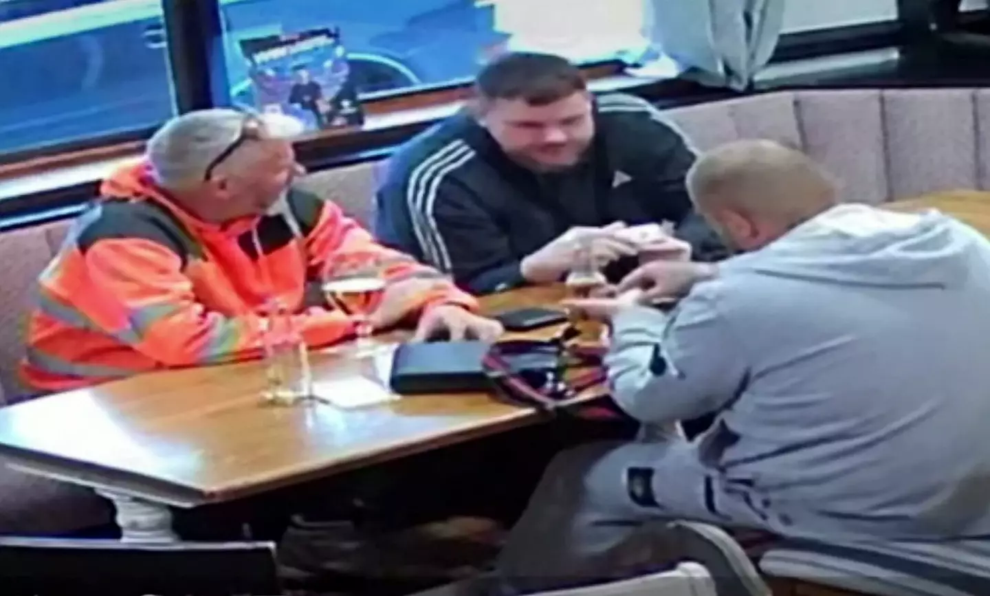 The footage shows a workman in a hi-vis jacket chatting with two mates at a table.
