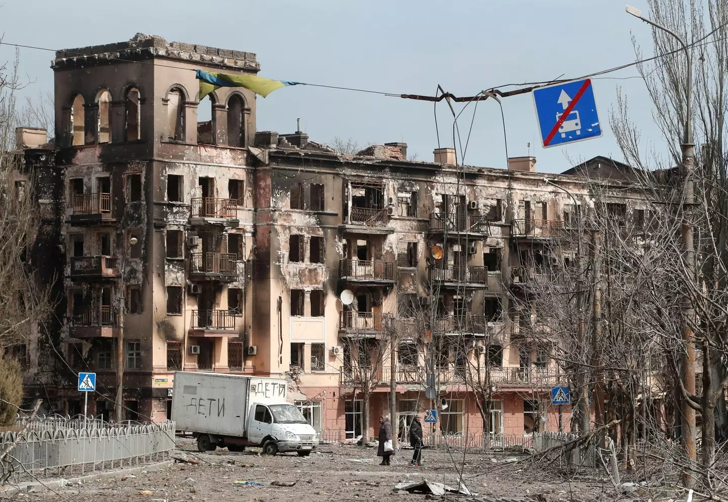 Locals walk along a street next to a building damaged during Ukraine-Russia conflict in the southern port city of Mariupol.