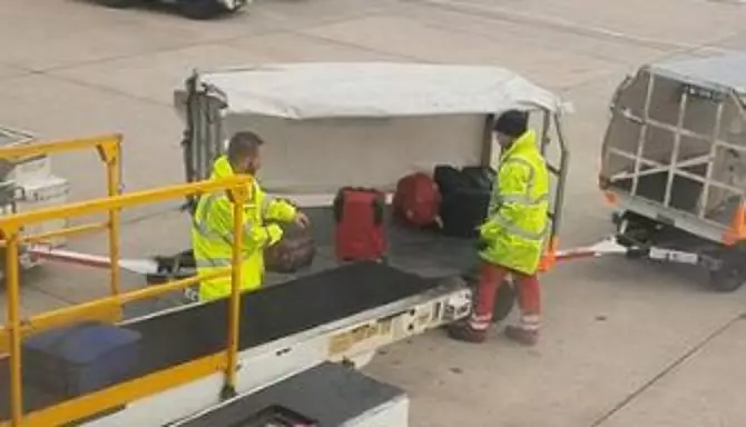 Baggage handlers carelessly fling suitcases onto a cart.