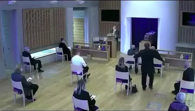 A funeral worker interrupts the service to tell them to move their chairs back (