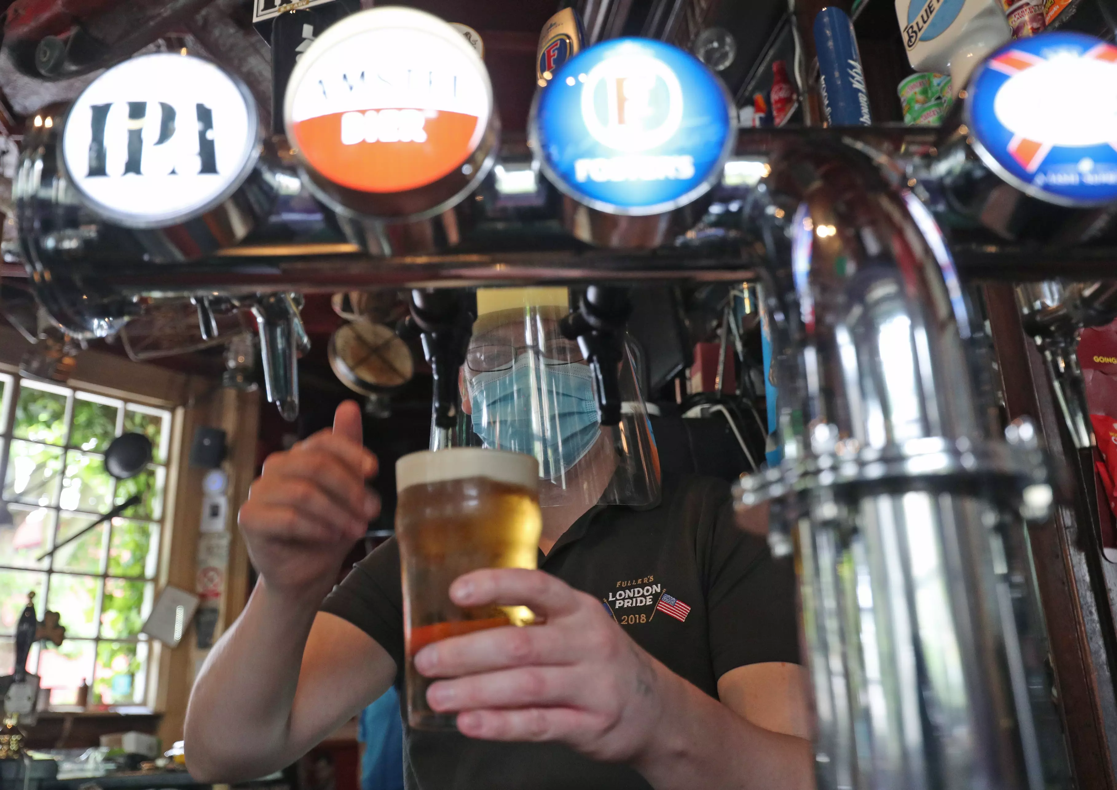 Barman Michael Fitzsimons wears PPE while pouring a pint during final preparations at The Faltering Fullback pub in North London.