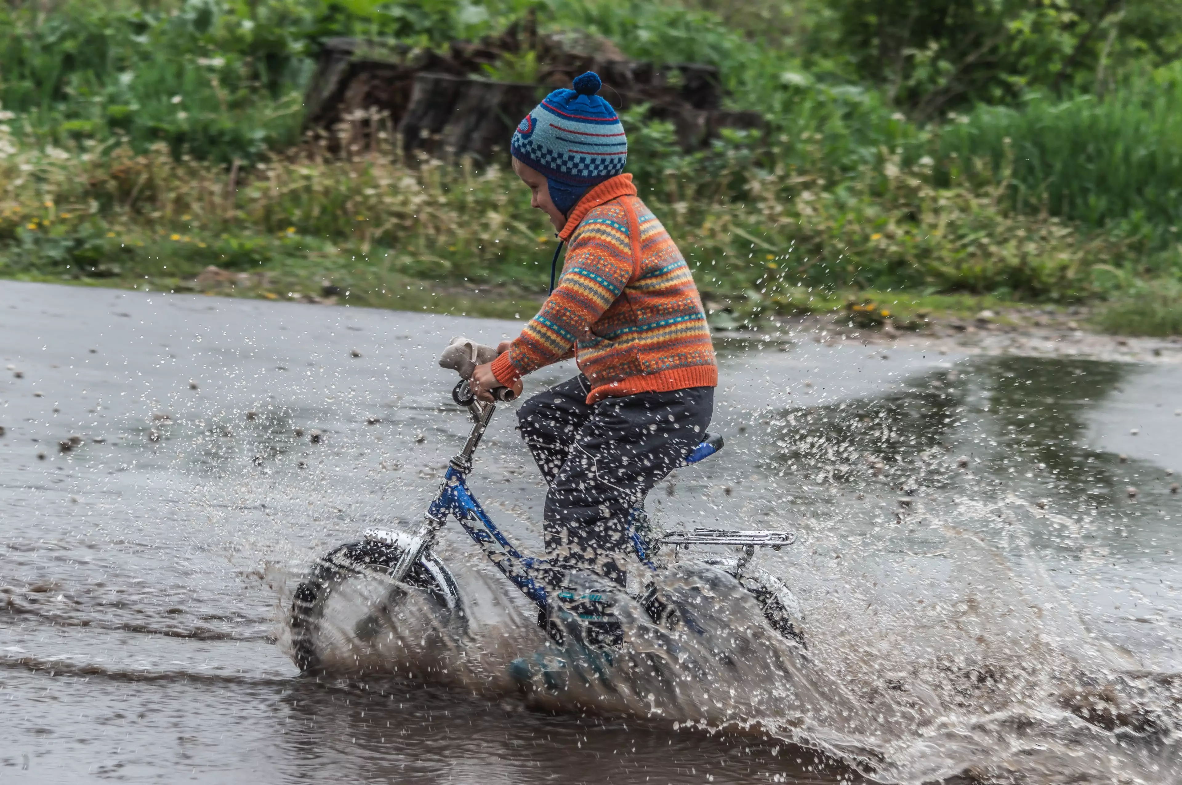 Boy rides his bike through a puddle after a storm. (