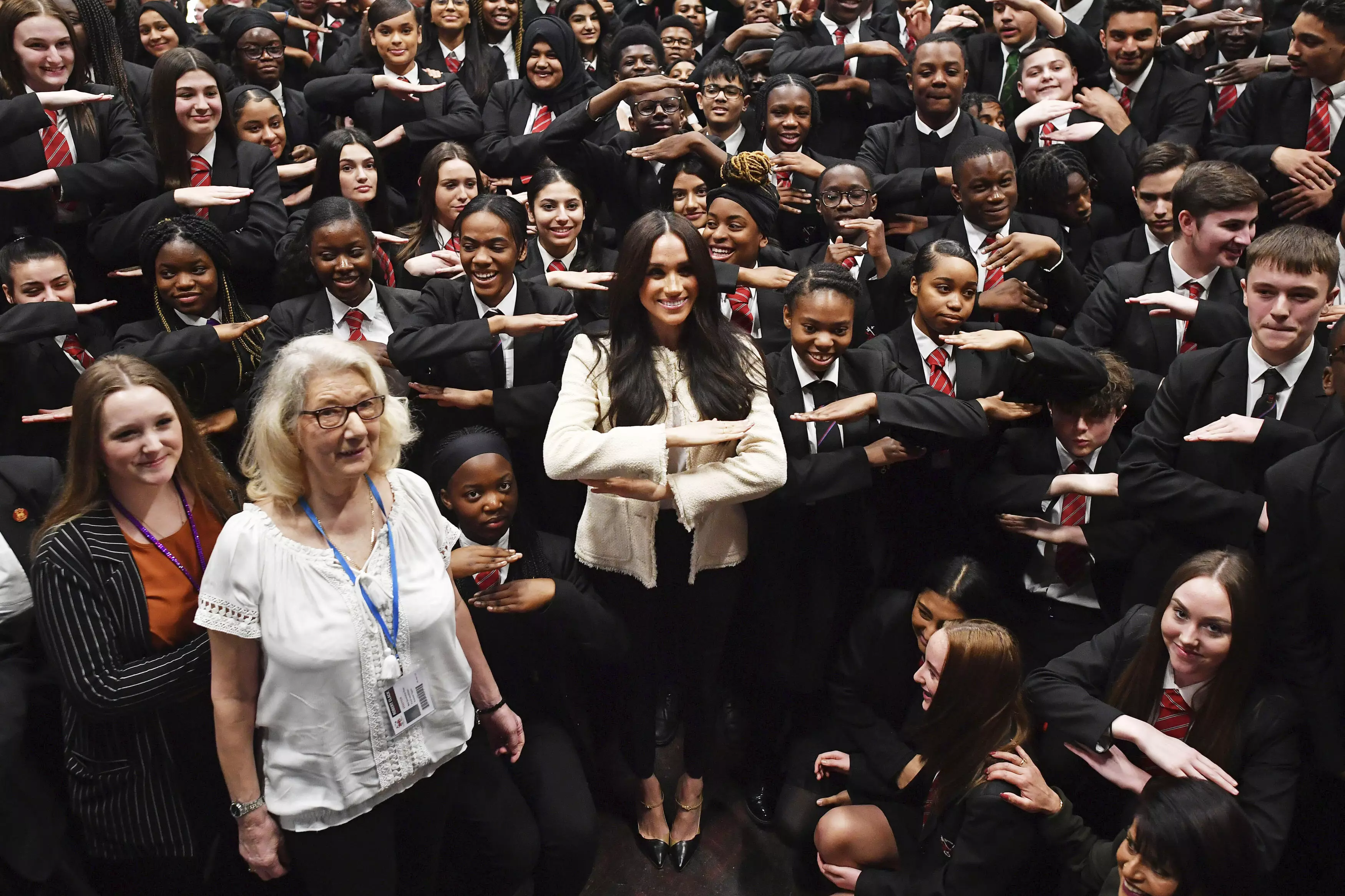 Meghan posing with school children making the equality sign.