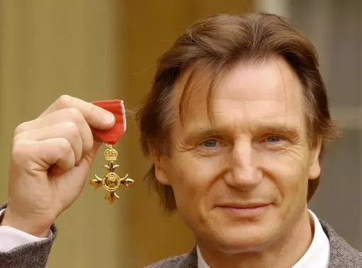 Liam Neeson holds his OBE in the forecourt of Buckingham Palace.