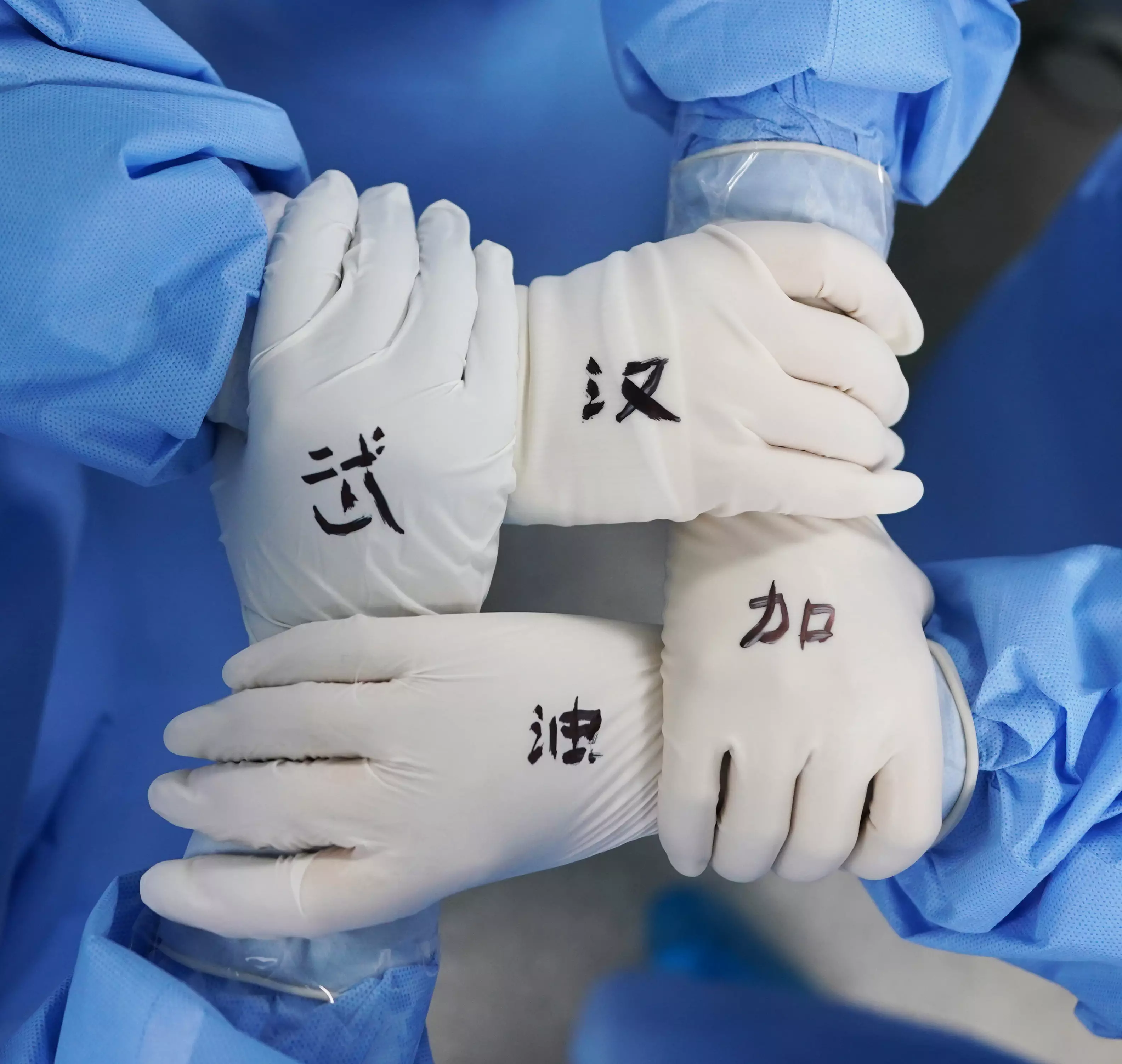 Nurses holding hands in surgical gloves with 'cheer up Wuhan' written on them.