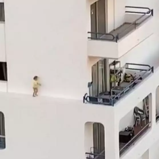 The small toddler can be seen running across the narrow ledge of an apartment complex. 