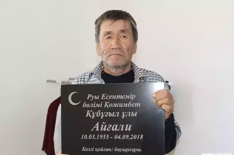 Aigali Supugaliev posed with his own gravestone and doesn't he look delighted to be alive?