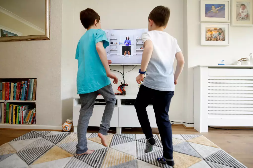 Two school kids exercising with the nation's new virtual PE teacher, Joe Wicks.
